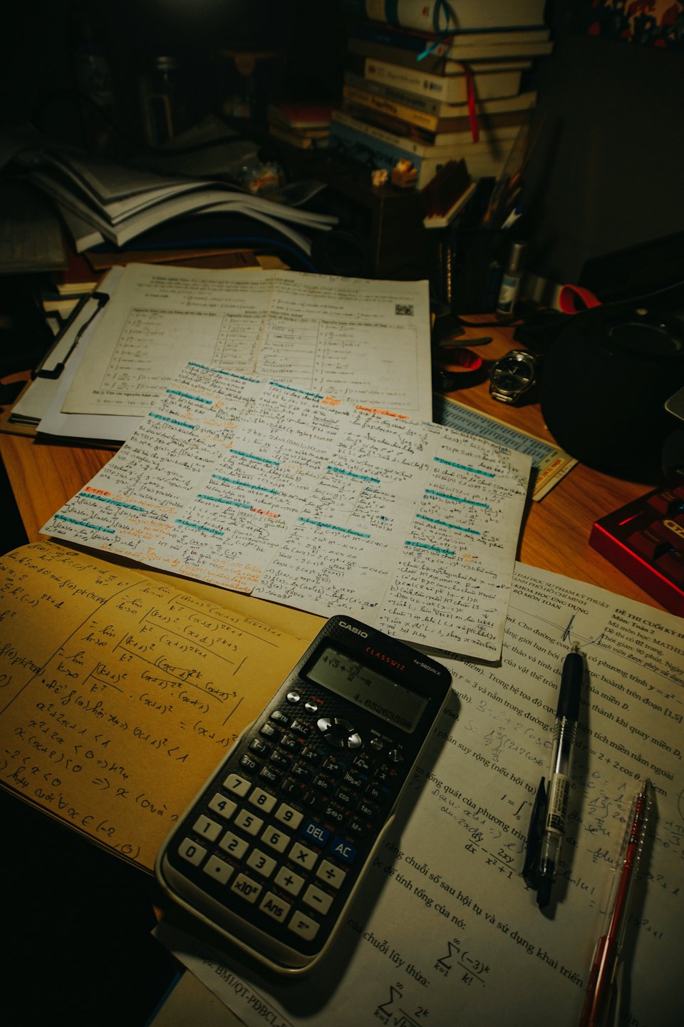 Notatniki, podręczniki i papiery z równaniami matematycznymi na zagraconym biurku.