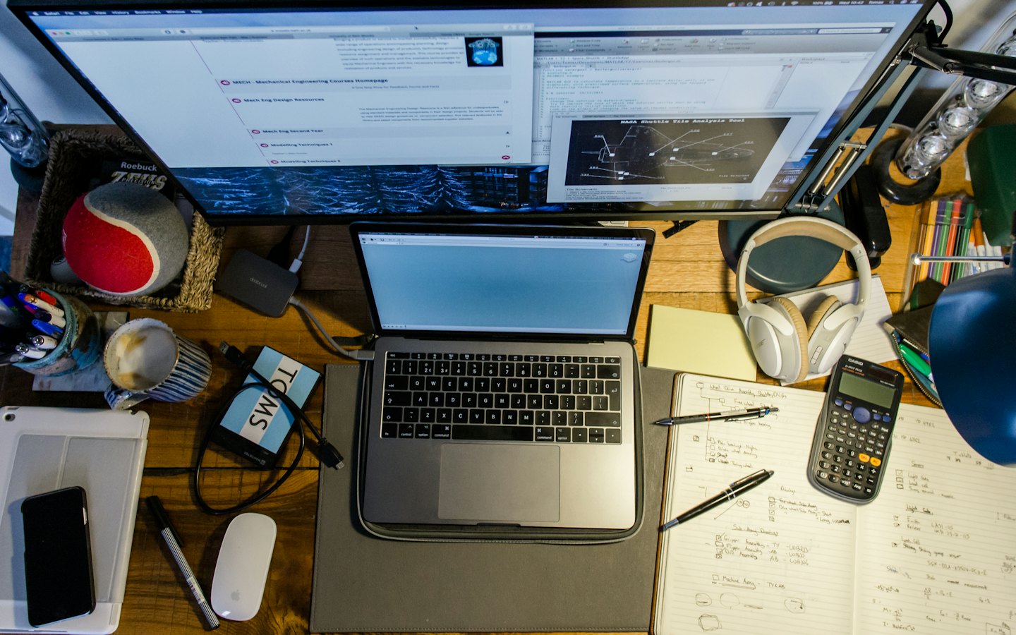 Laptop i zewnętrzny monitor na zagraconym drewnianym biurku.